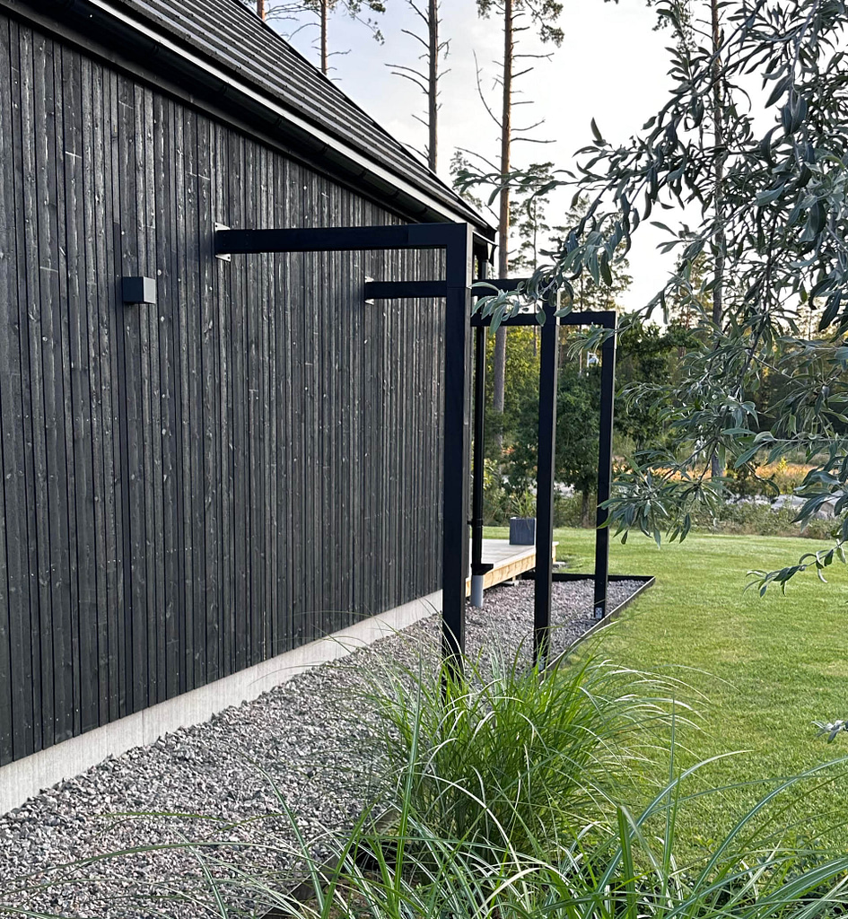 Svart pergolagång med pergolabeslag från Wernamo Design längs modern husfasad