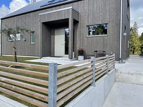 Lågt staket på en mur, med galvade staketstolpar och liggande reglar i trä.