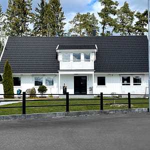 Svart underhållsfritt staket i metall framför en stor vit villa.