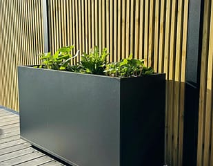 Plant Box Flex - rostfritt planteringskärl - svensktillverkat från Wernamo Design. Står framför Ribbstaket Borgen.