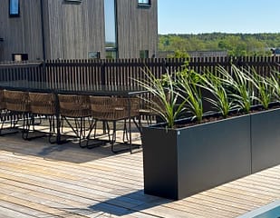 Rumsavdelare på stort trädäck. Plant Box i svart matt lack från Wernamo Design med vippande gräs.