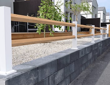 Vitt lågt staket med träreglar ovanpå en mur.