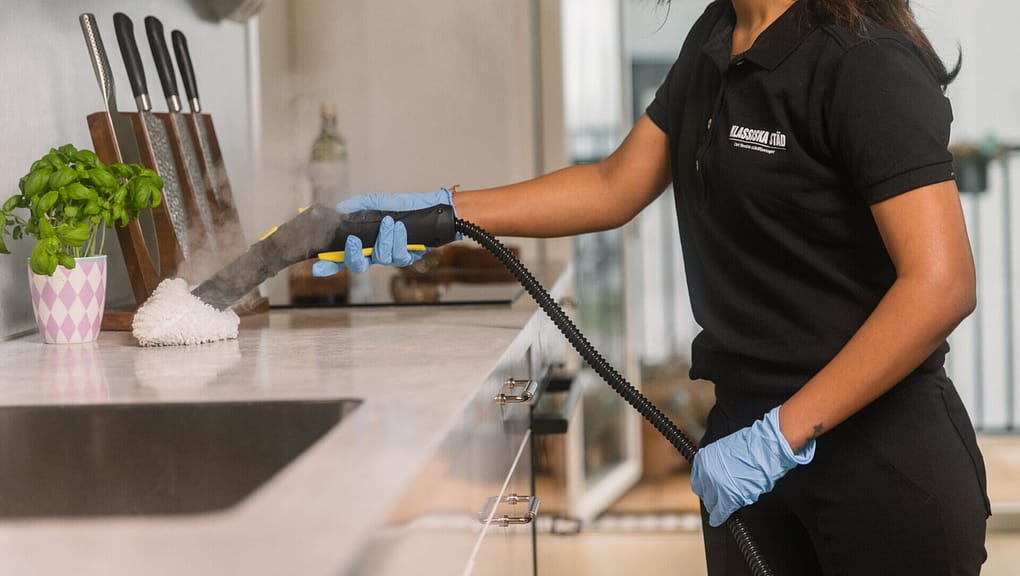 Kvinna städar diskbänk med ångmaskin.
