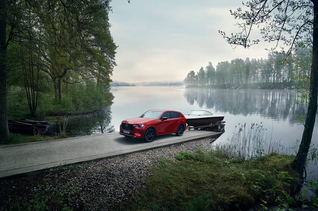 En röd Mazda med båt på släp lastar i båten i en sjö.
