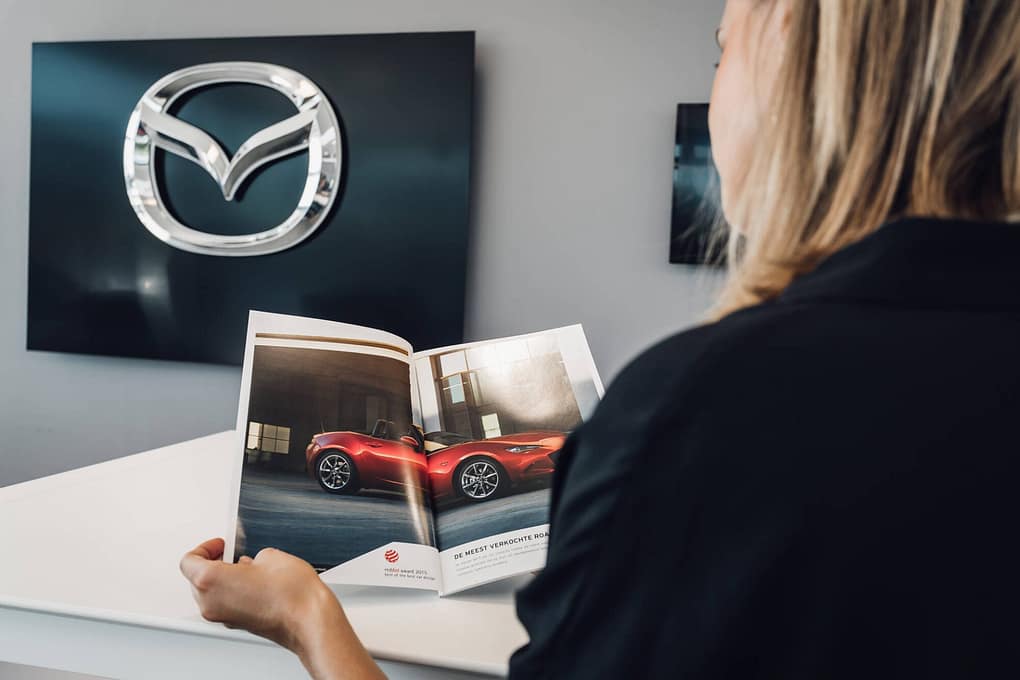 En kvinna bläddrar i ett magasin från Mazda. I bakgrunden syns Mazda-logotypen på en vägg.