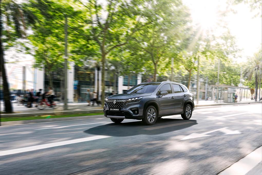 En svart Suzuki S-Cross kör på en väg i en stadskärna i solljuset.