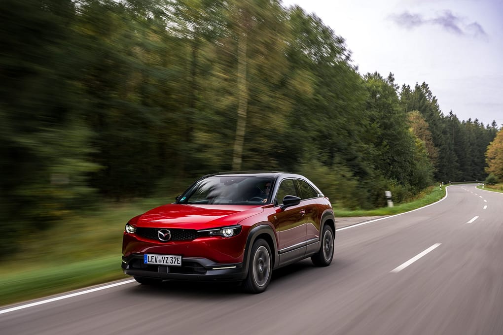 En röd Mazda MX-30 R-EV körandes på en landsväg omringad av skog.
