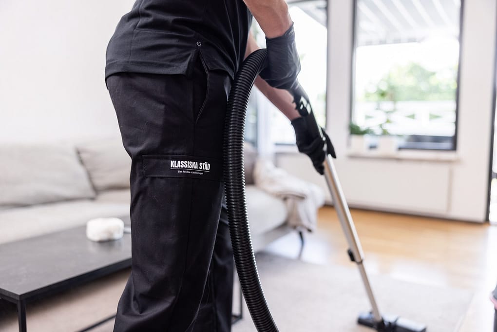 Städpersonal från Klassiska Städ dammsuger ett vardagsrum med professionell utrustning, iförd företagets svarta arbetskläder.