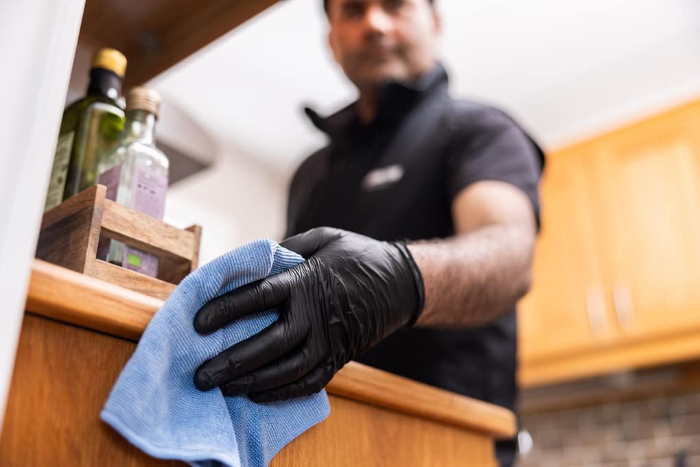 Städare från Klassiska Städ torkar av en köksbänk i trä med en blå mikrofiberduk, iförd svarta handskar.