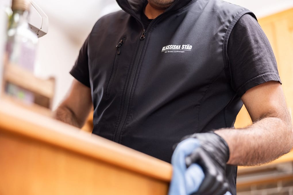 Städare från Klassiska Städ torkar av en köksyta med blå mikrofiberduk, iförd svart arbetsväst med logotyp.