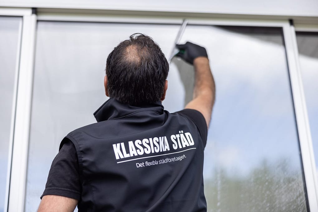 Fönsterputsare med företagskläder som putsar fönster utifrån.