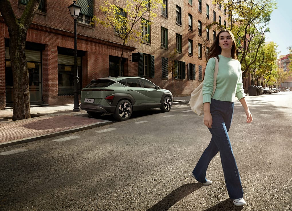 En kvinna i mintfärgad tröja går bort från en mintgrön Hyundai KONA som står parkerad på en gata i stadskärnan.