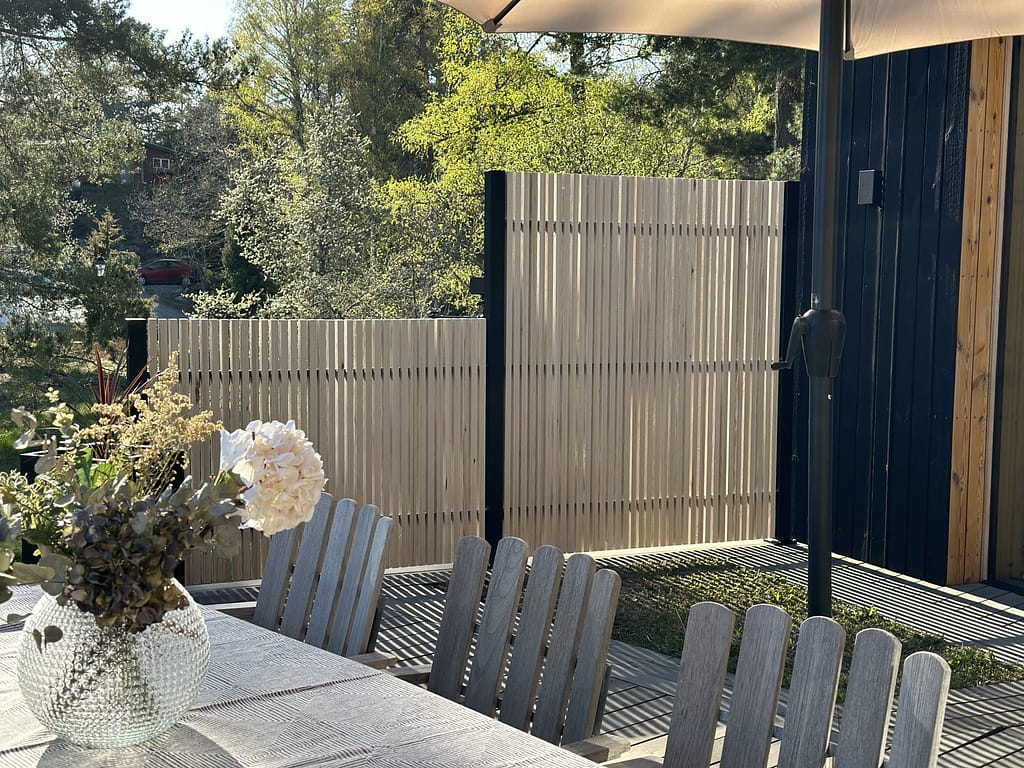 Staket i två höjder, med svarta stolpar och stående träribbor.