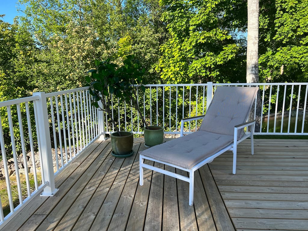 Vitt staket i modell Herrestad med solstol i förgrund.