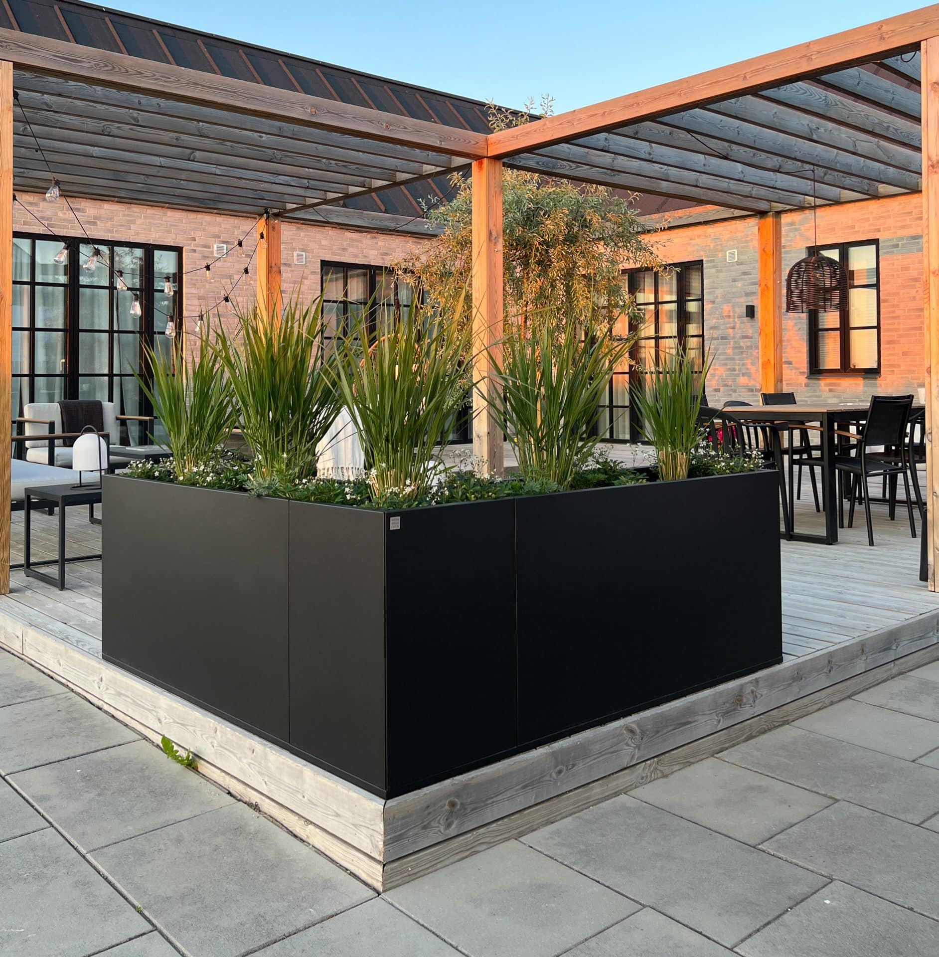 Planteringskärl i form av Plant Box ramar in hörnet på en uteplats.