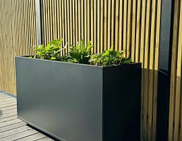 Plant Box Flex - rostfritt planteringskärl - svensktillverkat från Wernamo Design. Står framför Ribbstaket Borgen.