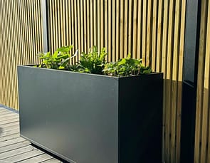 Plant Box Flex - rostfritt planteringskärl - svensktillverkat från Wernamo Design. Står framför Ribbstaket Borgen.