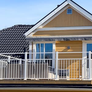 Balkongräcke i vitlackerad aluminium (RAL 9010) integrerat i klassisk sekelskiftesmiljö med Jotun 1124 Skagengul fasad och vitmålade snickerier.