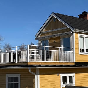 Vedligeholdelsesfrit altangelænder i aluminium, RAL 9010 hvid, monteret på hus med facade i Jotun 1124 Skagengul og hvide hjørnelister.