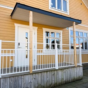 Vedligeholdelsesfrit stakit i RAL 9010 hvid aluminium omkring veranda, monteret mod facade malet i Jotun 1124 Skagengul med klassiske hvide detaljer.