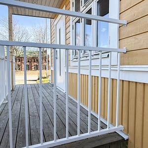 Detalj av balkongräcke i underhållsfri aluminium, RAL 9010 vitt, mot skagensgul träfasad målad i Jotun 1124 – traditionellt uttryck med vita knutar.