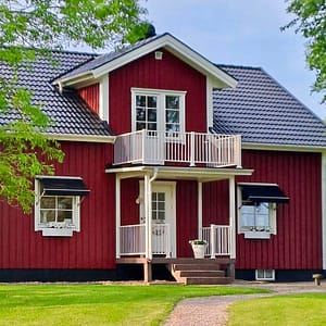 Lantligt falurött hus med vita knutar. Vitt underhållsfritt staket vid entré och på balkong.