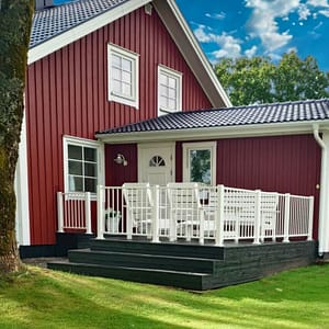 Uteplats i en lantlig miljö. Vitt staket till en faluröd villa.