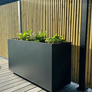 Plant Box Flex - rostfritt planteringskärl - svensktillverkat från Wernamo Design. Står framför Ribbstaket Borgen.