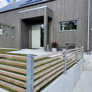 Lågt staket på en mur, med galvade staketstolpar och liggande reglar i trä.