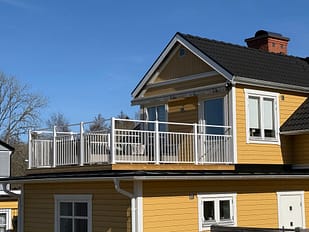 Vedligeholdelsesfrit altangelænder i aluminium, RAL 9010 hvid, monteret på hus med facade i Jotun 1124 Skagengul og hvide hjørnelister.