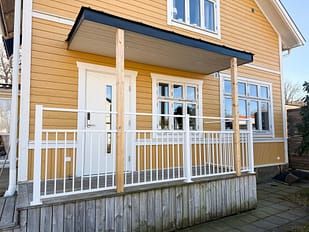 Vedligeholdelsesfrit stakit i RAL 9010 hvid aluminium omkring veranda, monteret mod facade malet i Jotun 1124 Skagengul med klassiske hvide detaljer.