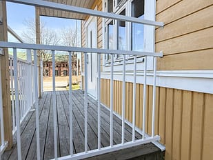 Detalj av balkongräcke i underhållsfri aluminium, RAL 9010 vitt, mot skagensgul träfasad målad i Jotun 1124 – traditionellt uttryck med vita knutar.