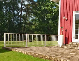 Vitt aluminiumräcke vid uteplats till ett rött hus med vita knutar.