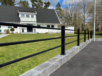 Svart staket med liggande rör framför en vit villa.