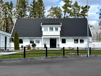 Svart underhållsfritt staket i metall framför en stor vit villa.
