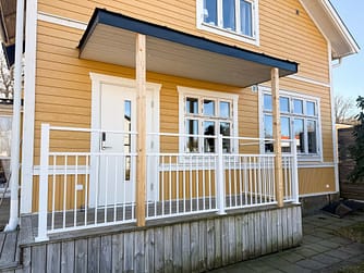 Vedligeholdelsesfrit stakit i RAL 9010 hvid aluminium omkring veranda, monteret mod facade malet i Jotun 1124 Skagengul med klassiske hvide detaljer.