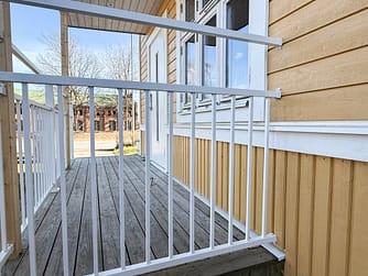 Detalj av balkongräcke i underhållsfri aluminium, RAL 9010 vitt, mot skagensgul träfasad målad i Jotun 1124 – traditionellt uttryck med vita knutar.