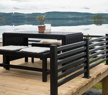 Svart staket på trädäck som har utsikt över en sjö.