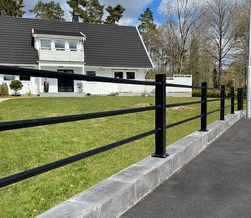 Sort hegn med vandrette rør foran en hvid villa.