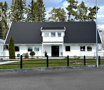 Sort vedligeholdelsesfrit metalhegn foran en stor hvid villa.