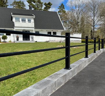 Sort hegn med vandrette rør foran en hvid villa.