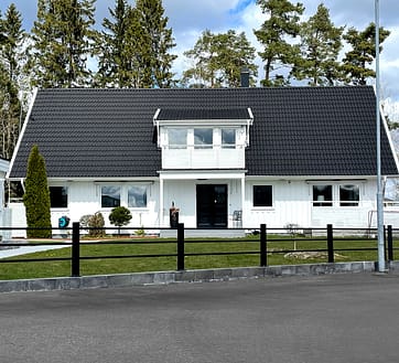 Sort vedligeholdelsesfrit metalhegn foran en stor hvid villa.