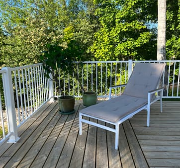 Vitt staket i modell Herrestad med solstol i förgrund.