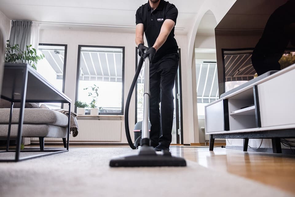 Städare från Klassiska Städ dammsuger en ljus matta i ett modernt vardagsrum med stora fönster.